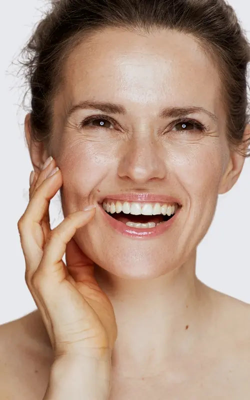 Woman with a bright smile touching her face against a white background